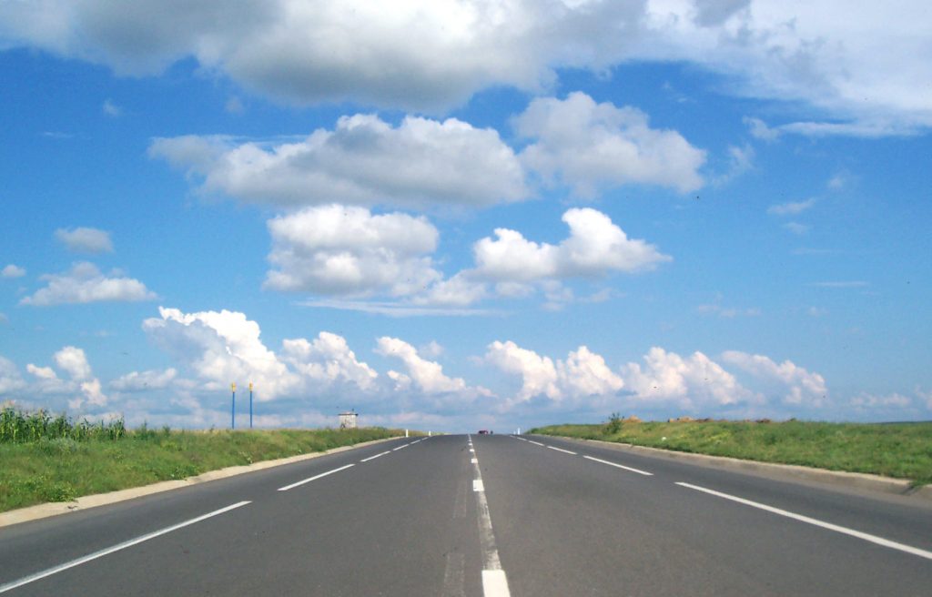 rodovia com céu azul e nuvens brancas com área verde dos dois lados