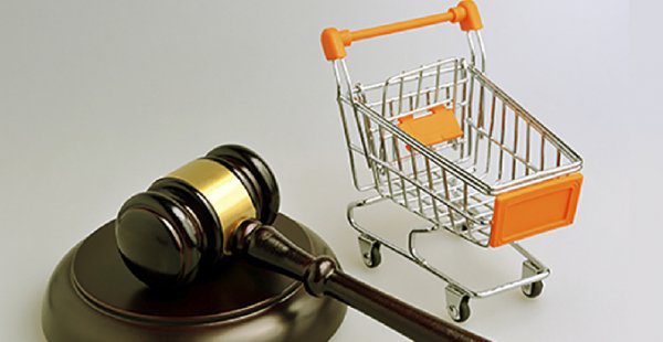 Martelo de juiz marrom ao lado de miniatura de carrinho de compra de supermercado com detalhas em laranja